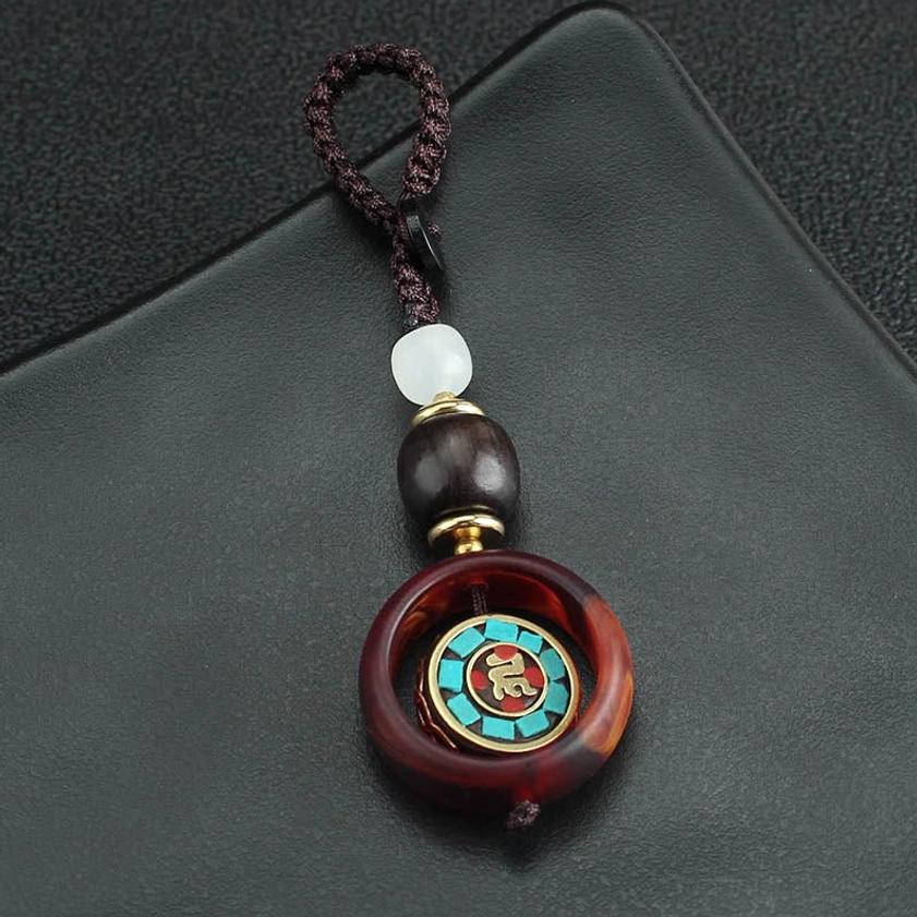 Front close-up of ebony wood Buddhist keychain charm with metallic and wooden bead accents on black leather background