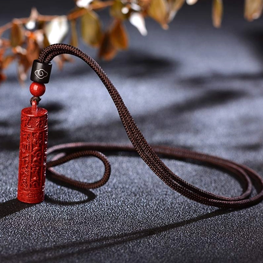 Red cinnabar mantra pendant necklace angled on dark table with natural foliage background, showcasing neat cord loop and pendant detail