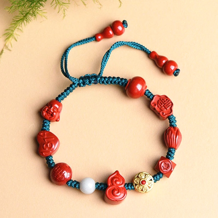 Flat lay photography of cinnabar Buddhist prayer bracelet with emblem beads, gold charm, and teal string on natural background