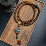 Schima wood and great bright mantra Buddhist necklace with coconut shell beads and copper charm displayed on wooden tray