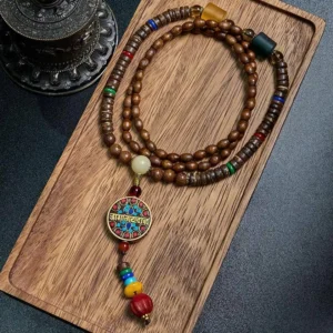 Schima wood and great bright mantra Buddhist necklace with coconut shell beads and copper charm displayed on wooden tray