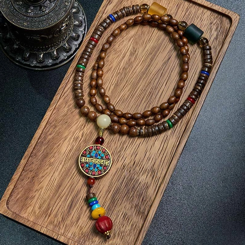Schima wood and great bright mantra Buddhist necklace with coconut shell beads and copper charm displayed on wooden tray