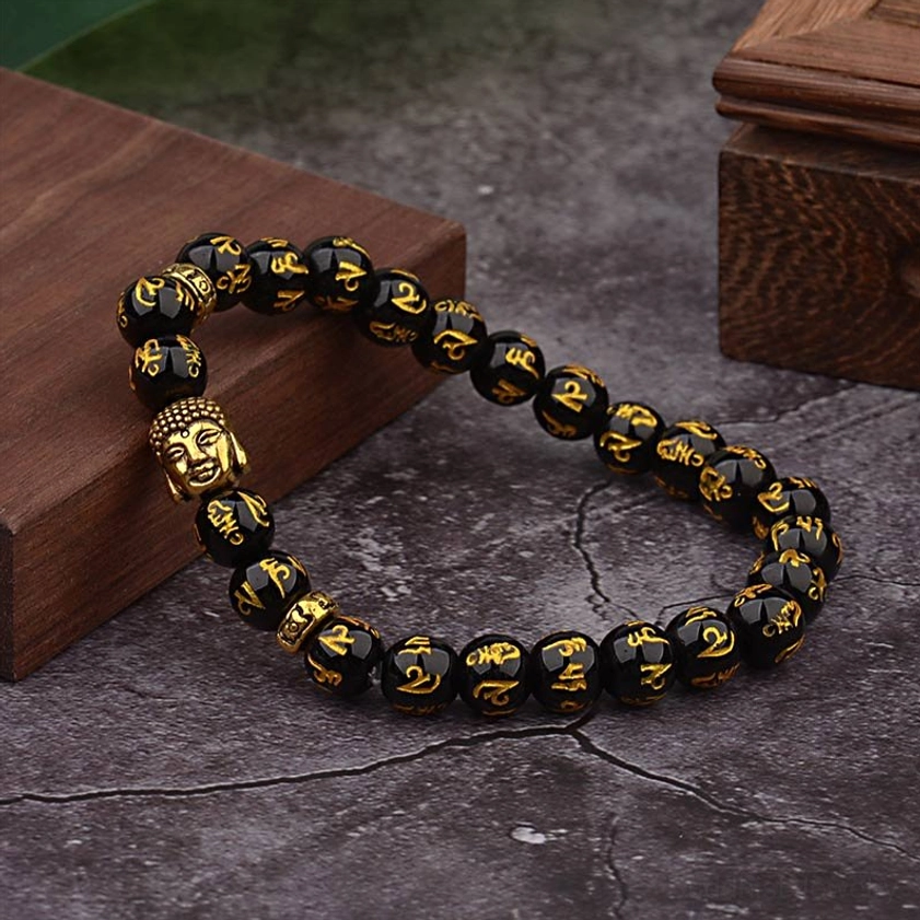 Black agate Om Mani Padme Hum bracelet with gold-plated Buddha bead on wooden prop, lifestyle angle shot