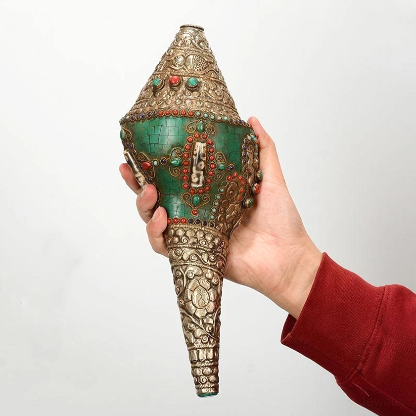 Handheld Buddhist conch shell decoration front view, person wearing red sleeve displaying the sacred Shankha ornament against white background