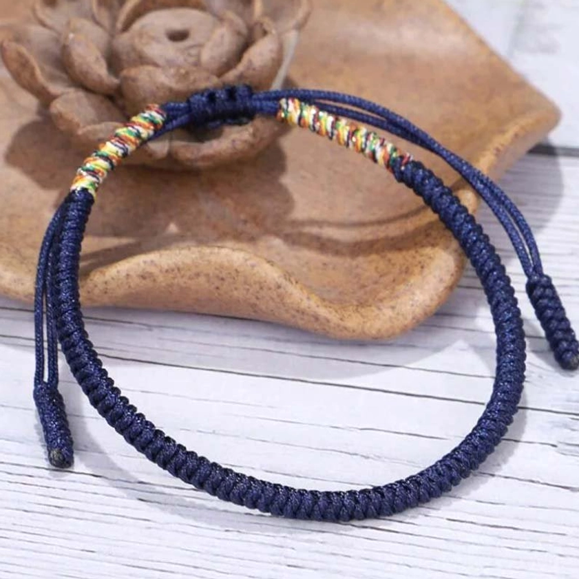 Tibetan style braided copper bracelet with multicolored trim and tassel ends on lotus decor wooden tray