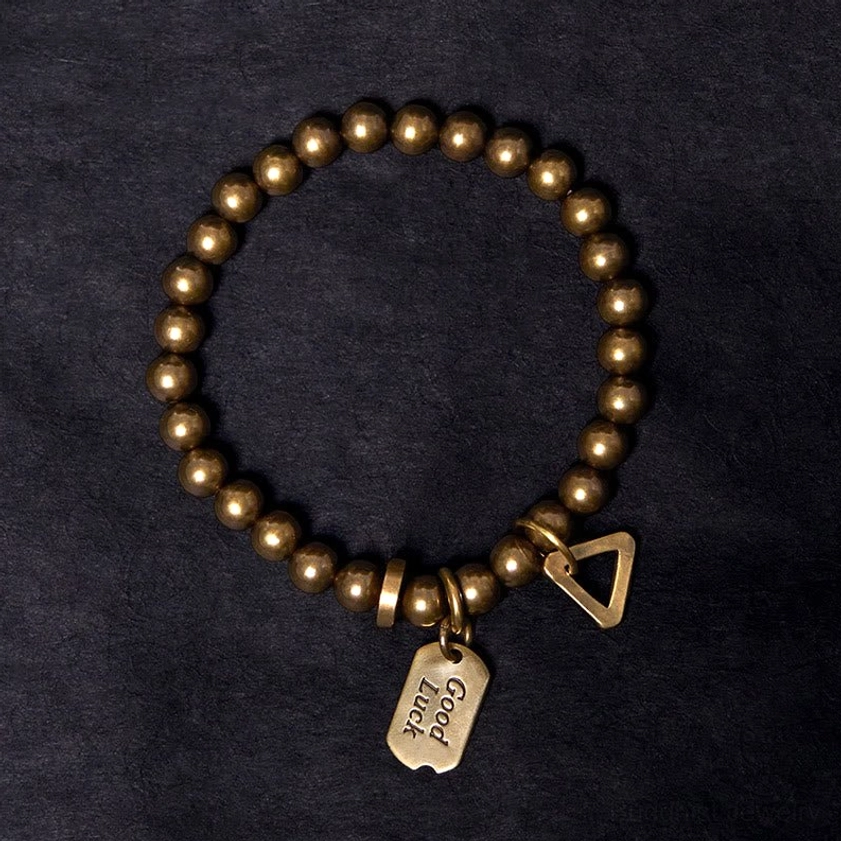 Top-down view of handmade copper Buddhist bracelet with Good Luck tag and decorative triangle clasp