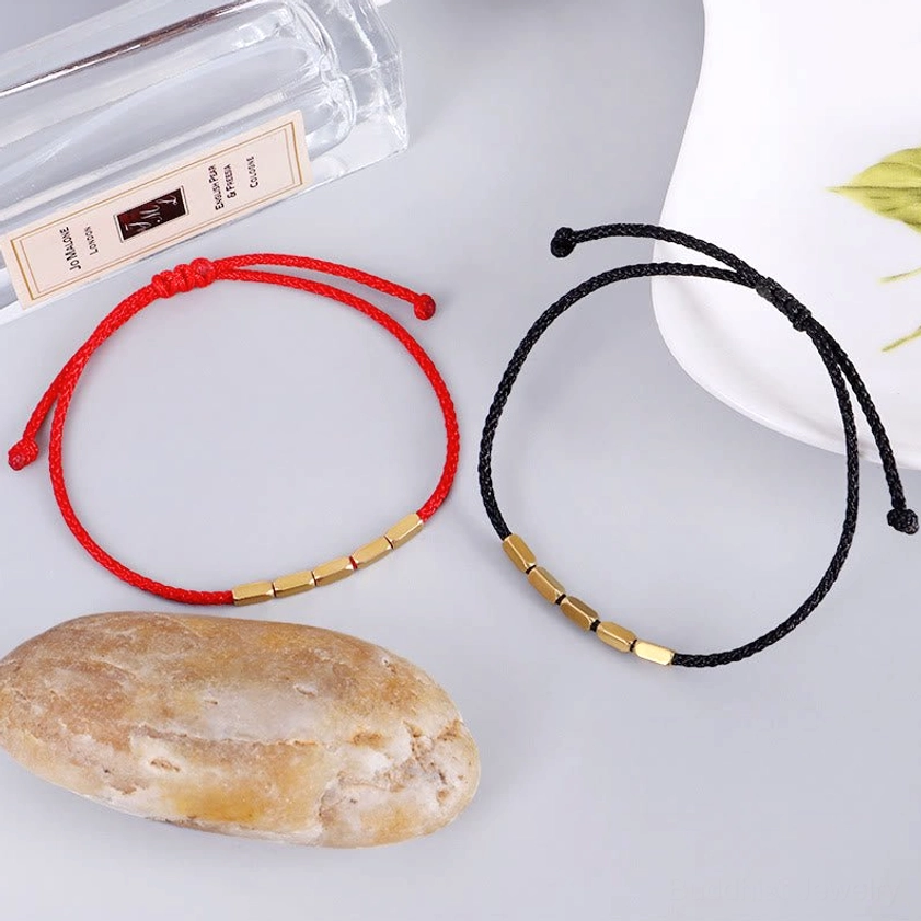 Red and black Buddhist protection bracelets displayed on styled desktop with natural stone and lifestyle accessories