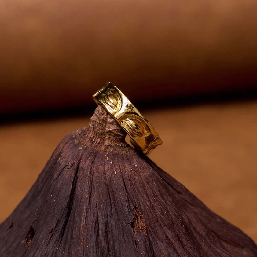 Single Buddha's eye adjustable copper ring resting on wooden cone display stand showcasing smooth golden metal texture