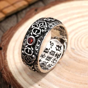 Handcrafted Buddhist copper ruby wealth ring with carved sutras, oblique view showcasing vintage silver finish and central red gemstone on wooden display