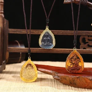 Multiple handcrafted Buddhist Liuli crystal pendants in vibrant colors displayed on wooden rack with bamboo mat, showing orange, blue, and green Buddha designs with gold metal frames