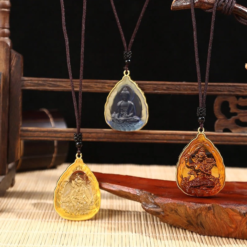 Multiple handcrafted Buddhist Liuli crystal pendants in vibrant colors displayed on wooden rack with bamboo mat, showing orange, blue, and green Buddha designs with gold metal frames