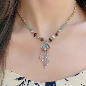 Buddhist copper tassel necklace with mixed stone beads worn on collarbone, showing detailed silver vintage charm with green enamel inlay against casual white halter top