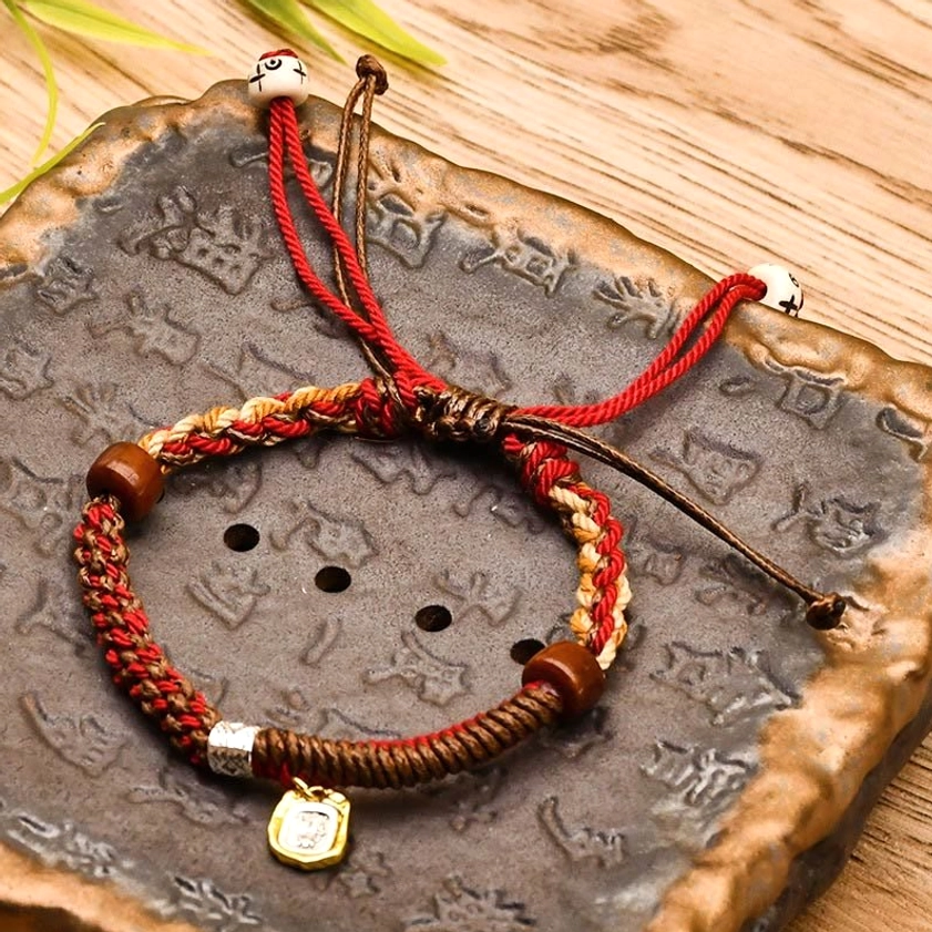 Dark red Buddhist wealth protection bracelet with wooden beads on carved stone display, adjustable drawstring closure