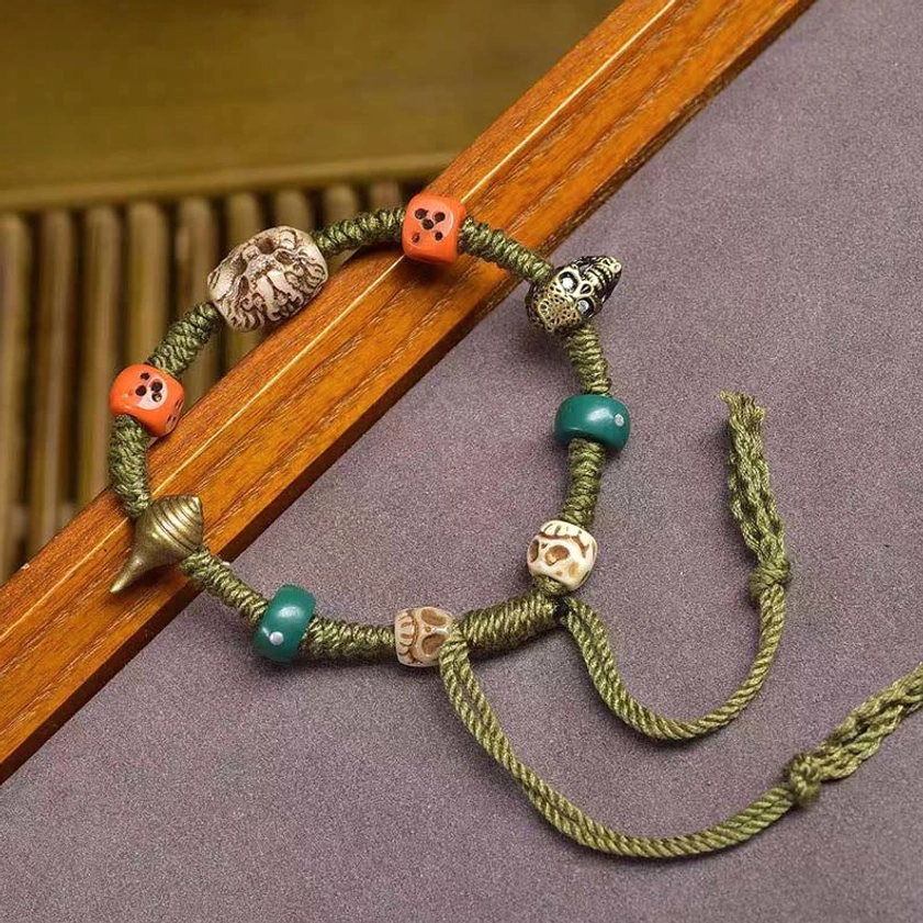 Side angle view of Buddhist dragon rope bracelet with decorative beads and metal conch charm detail