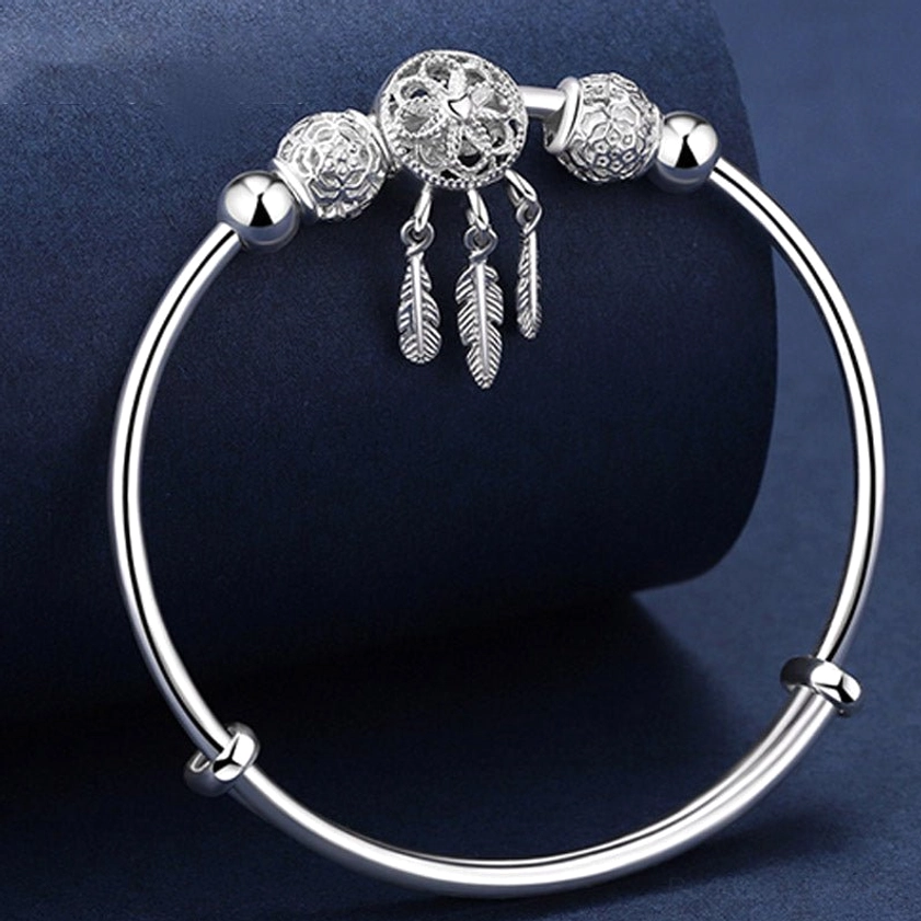 Front oblique view of silver dream catcher buddhist blessing bracelet with three feather pendants and bright polished silver finish on dark fabric background