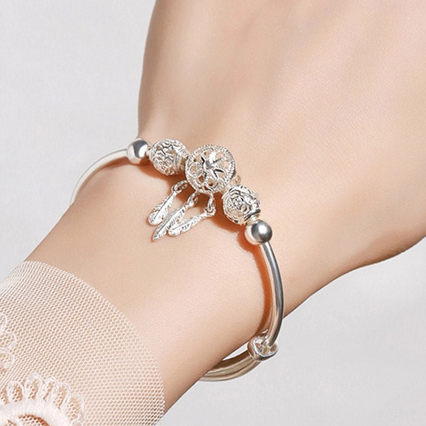 Dream catcher buddhist blessing bracelet worn on female wrist with delicate feather pendants and polished silver tone finish against lace background
