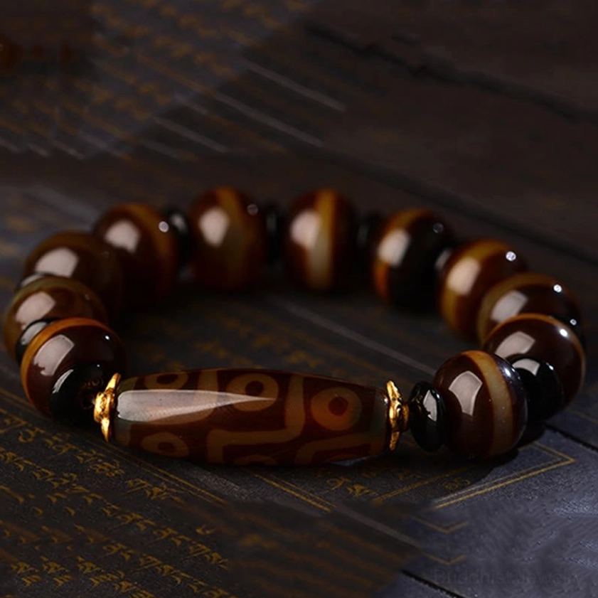 Tibetan dzi agate bracelet with polished brown beads and eye-patterned dzi bead with black spacers on vintage script mat