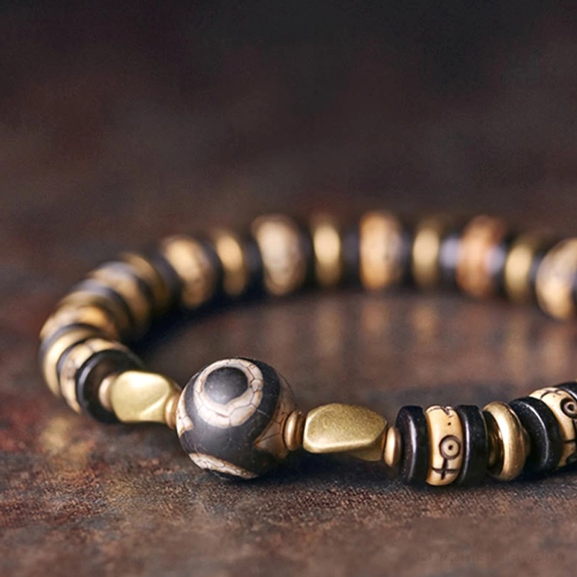 Close-up flat lay of Buddhist strength bracelet highlighting prominent eye Dzi bead, engraved symbols, and gold metal separators
