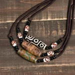 Collection of handmade Buddhist dzi bead necklaces with nine-eye patterns, various colors including black and brown, displayed on vintage wooden surface