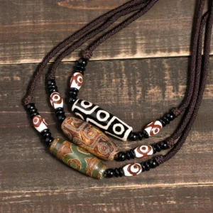 Collection of handmade Buddhist dzi bead necklaces with nine-eye patterns, various colors including black and brown, displayed on vintage wooden surface