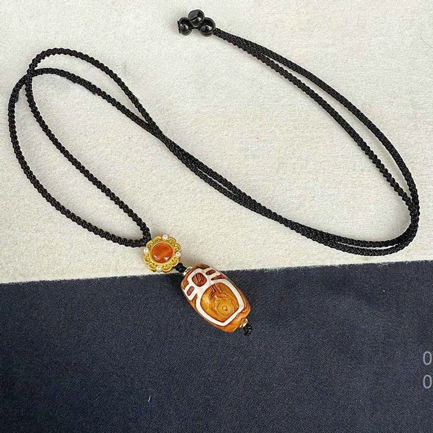 Nine-eye dzi bead Buddhist necklace with complete adjustable braided cord on fabric background