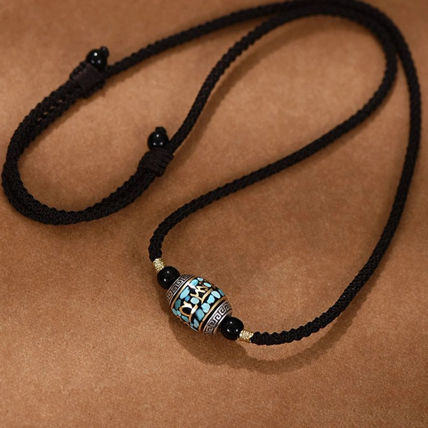 Rotatable Buddhist Dzi Bead pendant necklace flat lay showing adjustable woven cord