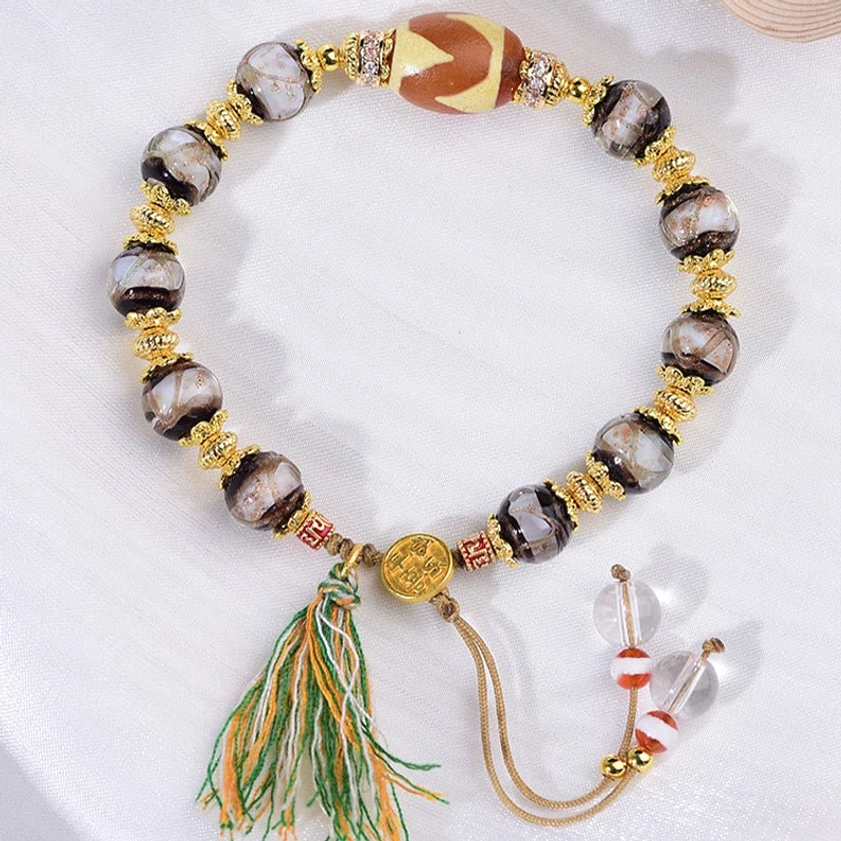 Liuli glass dzi bead bracelet flat lay with adjustable sliding knot tassel closure and crystal accents on white fabric