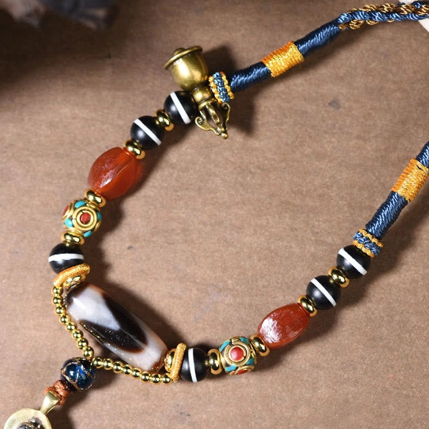 Dzi bead necklace partial view showing red agate beads and metal bell charm on wooden desk