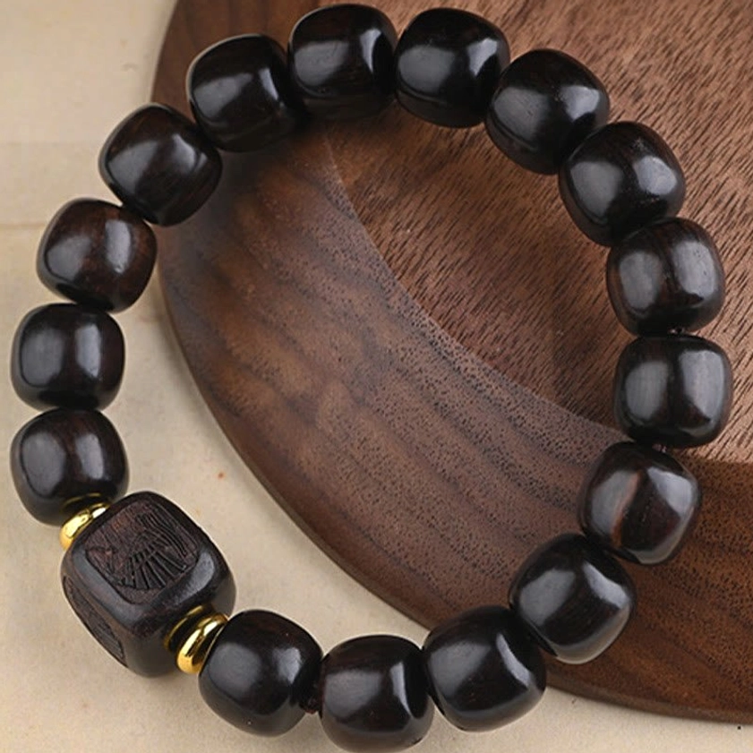 Natural ebony wood Buddhist bracelet with two carved wooden accents and gold spacers on round wooden tray