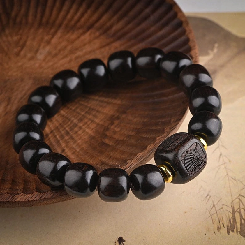 Handmade ebony wood Buddhist bracelet with square carved charm bead and polished dark wood finish on light backdrop