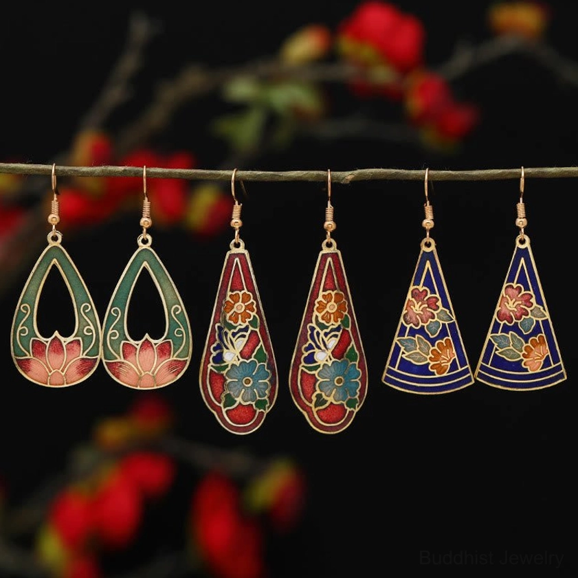 Assorted vintage Buddhist enamel earrings collection featuring lotus and flower patterns with gold frames on twig display