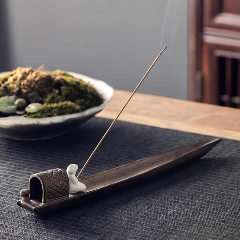 Side profile of brown ceramic Buddhist fishing boat incense burner with smoking incense on meditation table