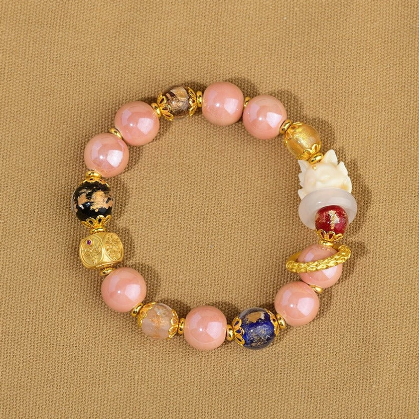 Nine-tailed fox incense ash glass bracelet fitted on woman's wrist with white sleeve, displaying pink beads and gold ring spacers, back angle view