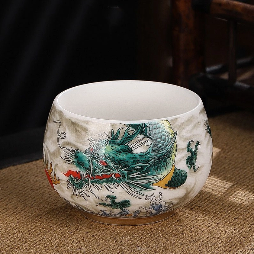 Side view close-up of green dragon ceramic tea cup with red sun and sea wave designs on white background