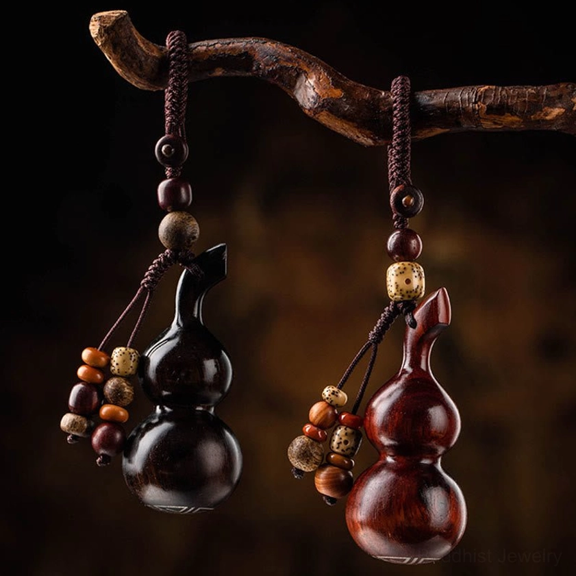Two sacred gourd keychains in red sandalwood and ebony, hanging from natural tree branch overhead view, showing beaded tassel decorations and traditional Buddhist craftsmanship