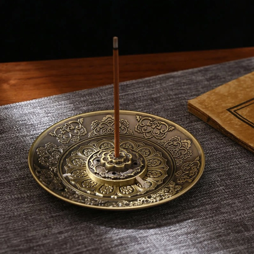 Buddhist incense burner with embossed decorative patterns displayed on wooden desk with linen mat, overhead view