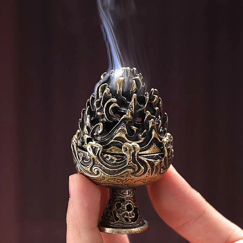 Handcrafted Buddhist incense burner held in fingers, front view showing intricate mountain relief carving and smoking cone incense