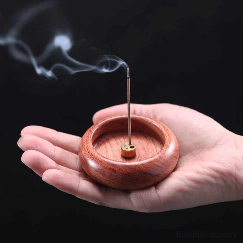 Warm reddish-brown wood Buddhist incense burner held in hand with smoking incense and brass base