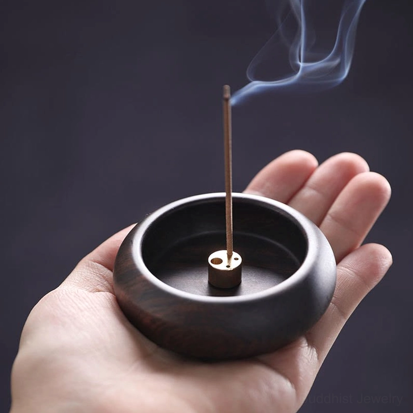 Round dark brown wood incense burner held in hand showing brass base and smoking incense stick