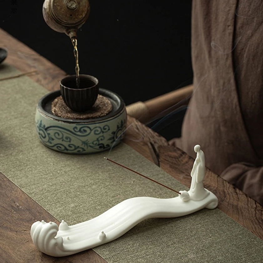 White ceramic Buddhist incense burner on tea table with matching tea brewing utensils and incense
