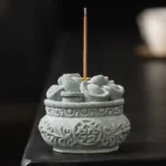 Buddhist sandstone incense burner with carved auspicious symbols and ingot decorations on dark wooden surface