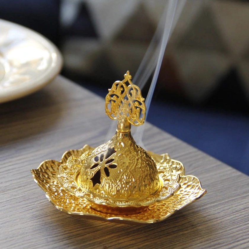 Gold incense holder with smoking incense and compact lotus tray, front side view on wooden surface