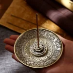 Handcrafted Buddhist incense holder with bronze finish and embossed lotus patterns held in palm, close-up view