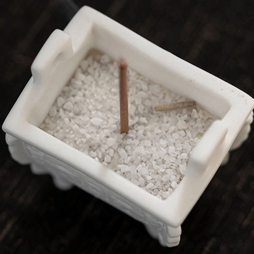 Top-down overhead view of Buddhist ceramic incense burner filled with white sand, holding two burning incense sticks