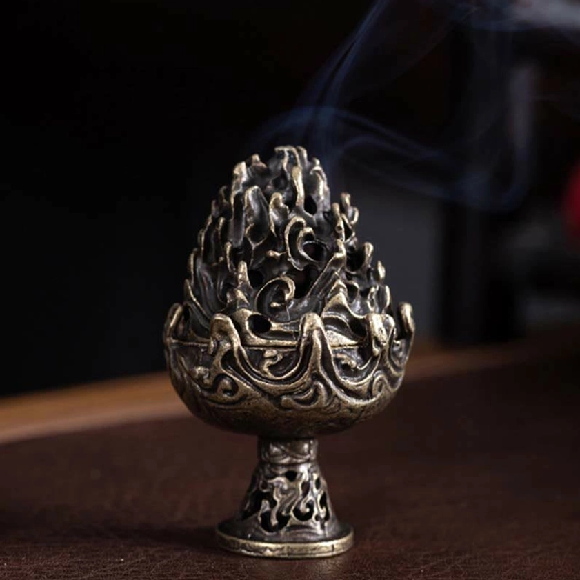 Buddhist incense holder side view with antiqued brass finish and ornate relief patterns, smoking incense burner on dark wooden table
