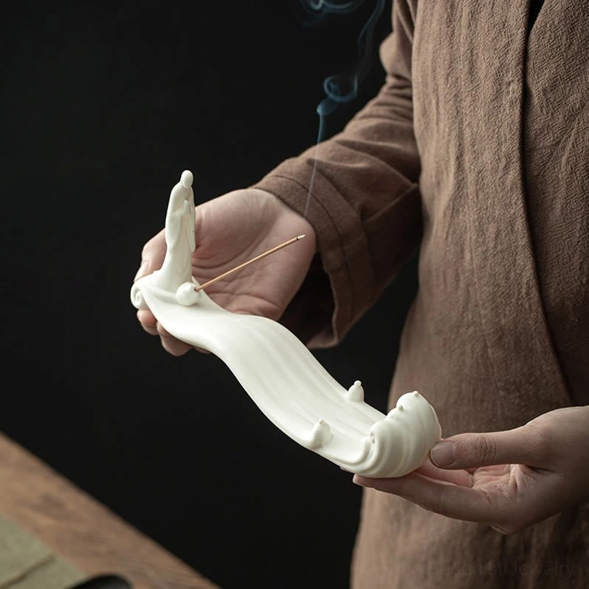Close-up of white ceramic Buddhist incense burner featuring seated monk figure and flowing wave design