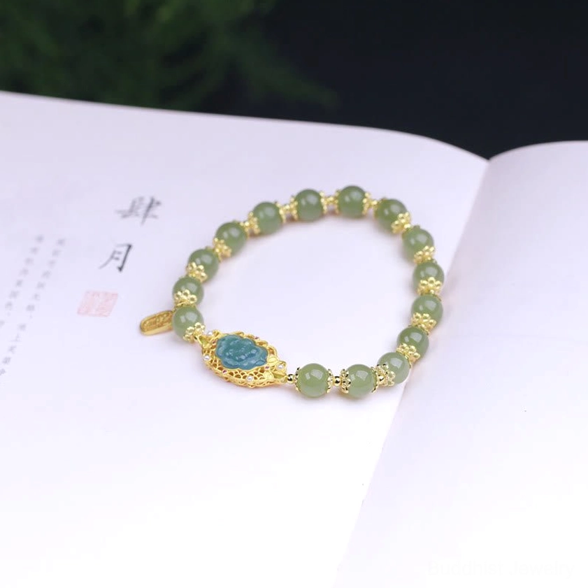 Jade lotus bracelet displayed on open Chinese calligraphy book, featuring gold metal accents, blue lotus central charm, and green jade beads
