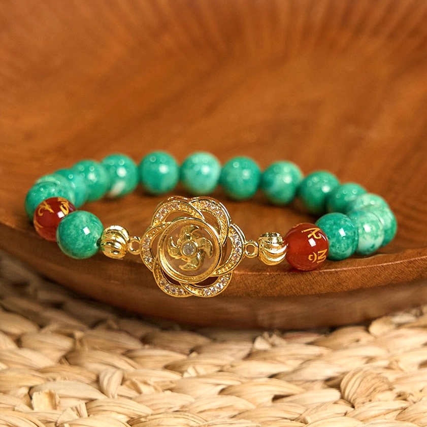 Green marbled jade beaded bracelet with red engraved agate and gold floral rotating charm on wooden bowl