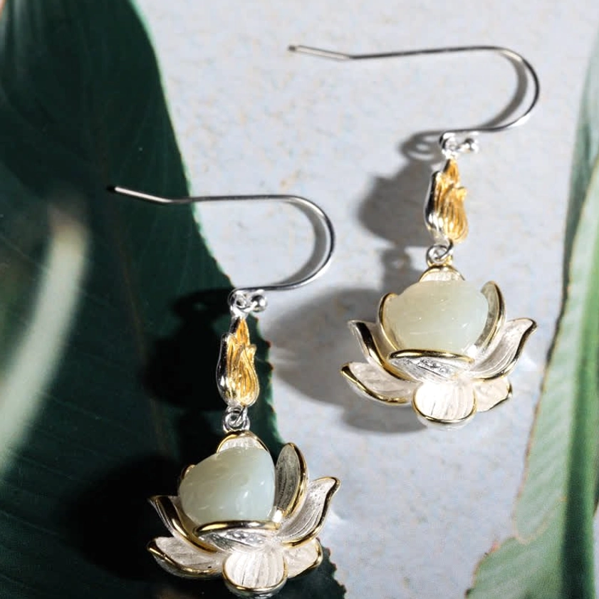 Handmade white jade lotus earrings at oblique angle on fabric and natural foliage background with silver ear hooks