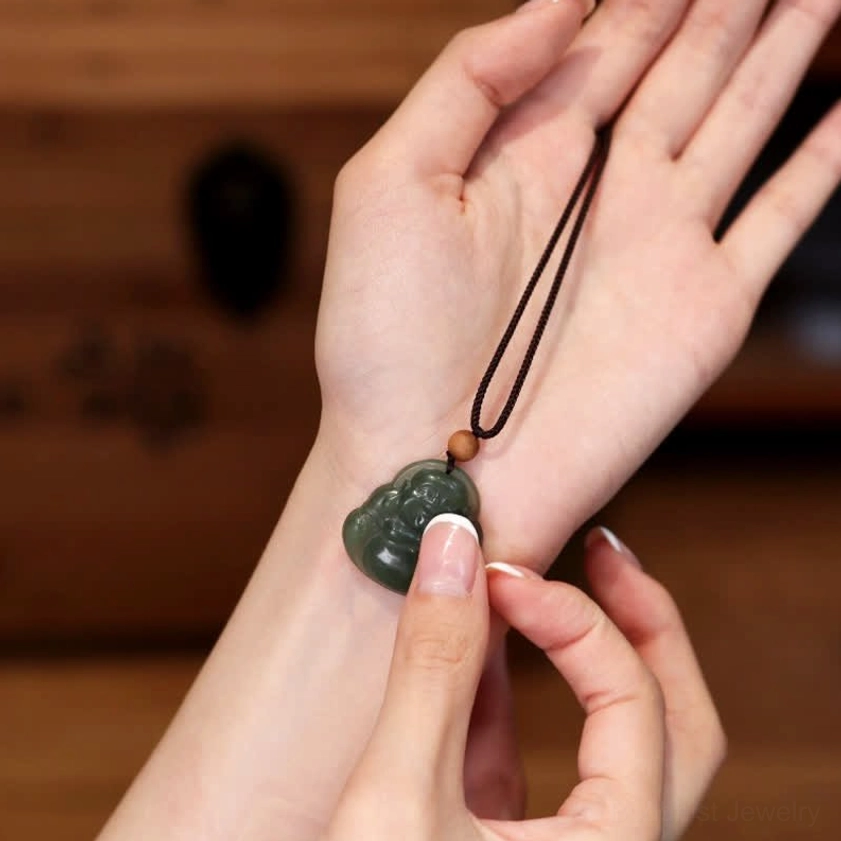Two hands adjusting Laughing Buddha jade necklace on inner wrist, demonstrating proper pendant placement and adjustable cord length